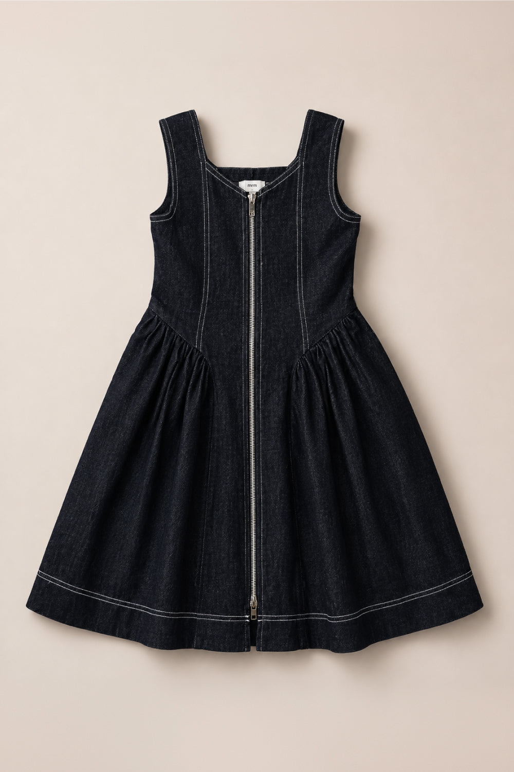 The Teen Edith Dress in Black by Ivy City Co is a sleeveless dark denim dress featuring a front zipper, square neckline, fitted bodice, flared skirt, and white contrast stitching. Crafted from a comfortable cotton-spandex blend for effortless movement, it’s shown laid flat on a beige background.