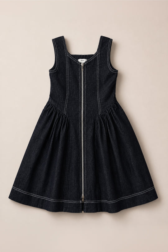 The Teen Edith Dress in Black by Ivy City Co is a sleeveless dark denim dress featuring a front zipper, square neckline, fitted bodice, flared skirt, and white contrast stitching. Crafted from a comfortable cotton-spandex blend for effortless movement, it’s shown laid flat on a beige background.