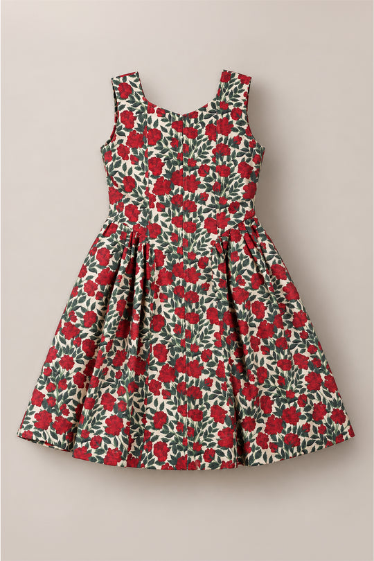 The Teen Edith Dress in Red Roses by Ivy City Co features a sleeveless design with a fitted bodice and pleated skirt. Showcasing a bold red rose floral pattern with green leaves on an off-white background, this dress stands out as the perfect choice for holiday parties.