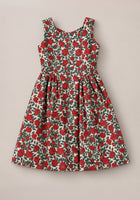 The Teen Edith Dress in Red Roses by Ivy City Co features a sleeveless design with a fitted bodice and flared skirt, adorned with vibrant red rose and green detailing on a white background. Displayed on a neutral surface, this dress is the perfect choice for your next holiday party.