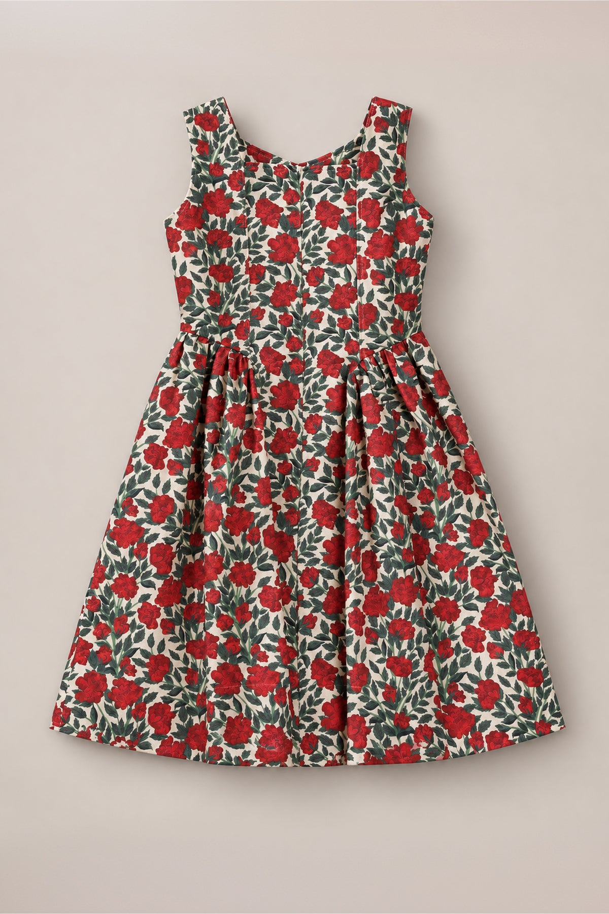 The Teen Edith Dress in Red Roses by Ivy City Co features a sleeveless design with a fitted bodice and flared skirt, adorned with vibrant red rose and green detailing on a white background. Displayed on a neutral surface, this dress is the perfect choice for your next holiday party.
