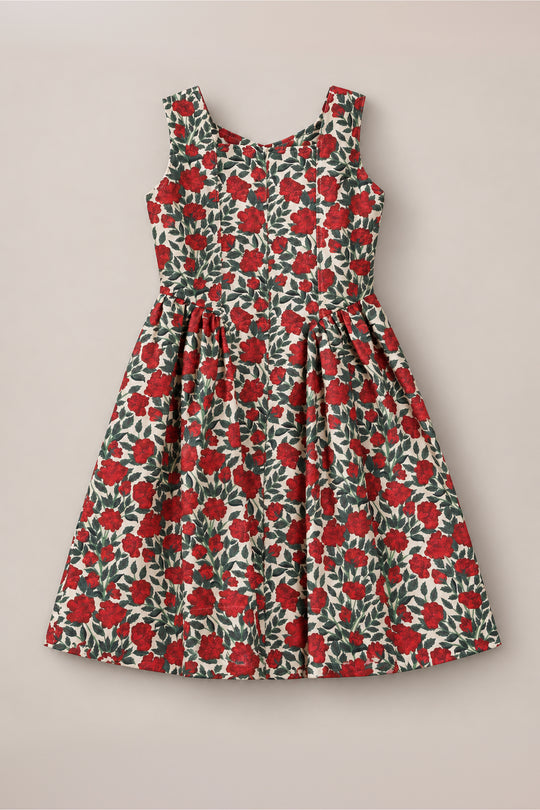 The Teen Edith Dress in Red Roses by Ivy City Co features a sleeveless design with a fitted bodice and flared skirt, adorned with vibrant red rose and green detailing on a white background. Displayed on a neutral surface, this dress is the perfect choice for your next holiday party.
