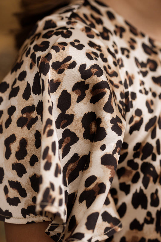 Close-up of a person wearing the Ivy City Co Teen Tallulah Dress in Leopard, featuring brown, black, and beige spots. The soft, smooth fabric is highlighted in the image, with a focus on the shoulder and stylish flutter sleeve detail.