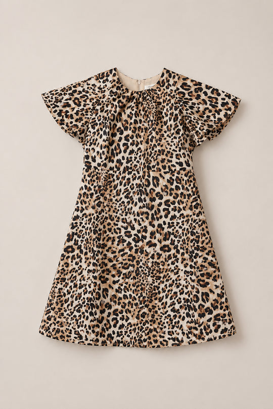 The Ivy City Co Teen Tallulah Dress in Leopard is a stylish knee-length, short-sleeve midi dress featuring a playful brown, black, and tan leopard print pattern. Displayed on a neutral background, this flutter sleeve dress is the perfect addition to any teen’s wardrobe.