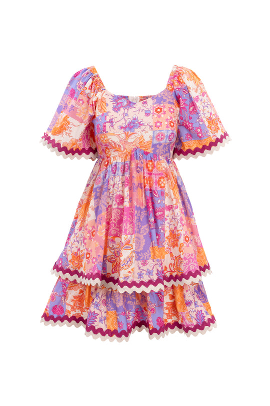 The Ivy City Co Tessa Dress in Pink Floral Tile is a short-sleeved, maternity-friendly dress with vibrant pink, purple, orange, and red patchwork and zigzag trim for effortless style.