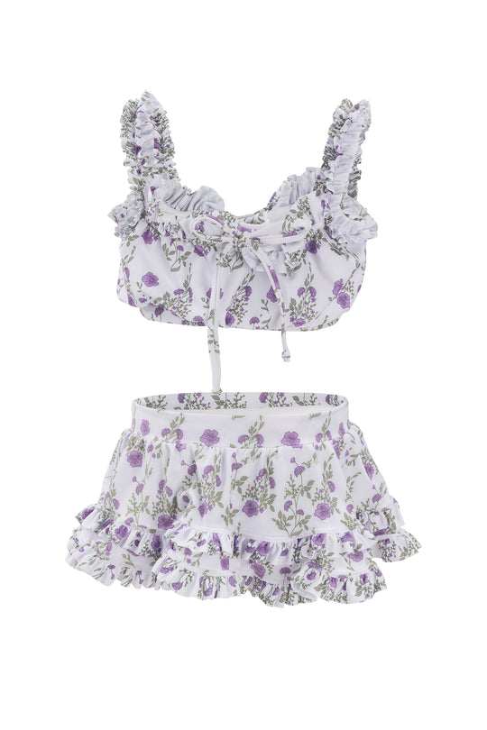 The Mini Rita Ruffle Skirt in Maeve Floral by Ivy City Co is a two-piece set with a ruffled crop top and matching mini skirt, both in white fabric with a purple floral print and shoulder straps.
