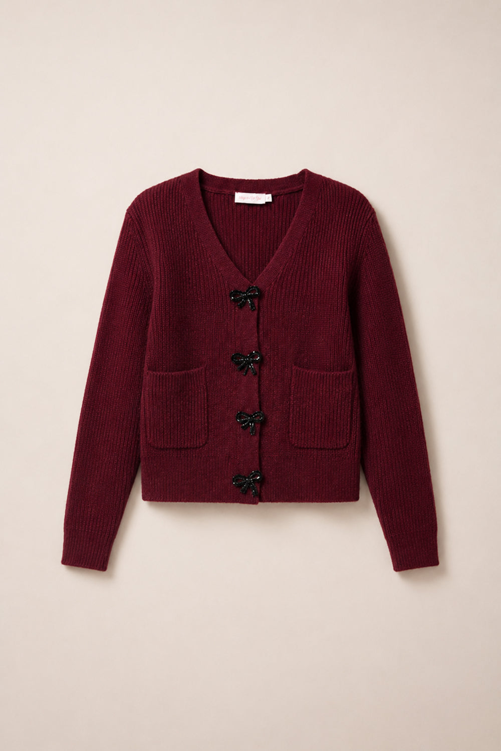 The Theo Sweater in Burgundy by Ivy City Co is a cozy fall cardigan featuring a V-neck, two front pockets, and four black bow-shaped button closures down the center. Crafted from an acrylic-nylon blend sweater material, it combines comfort and style—perfect for crisp autumn days.