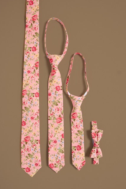 Four Ivy City Co “Ties in Pink Vintage Poppies”—long, medium, child-sized neckties, and a small bowtie—are displayed vertically on tan, perfect for family matching or spring photos with their charming rose pattern.