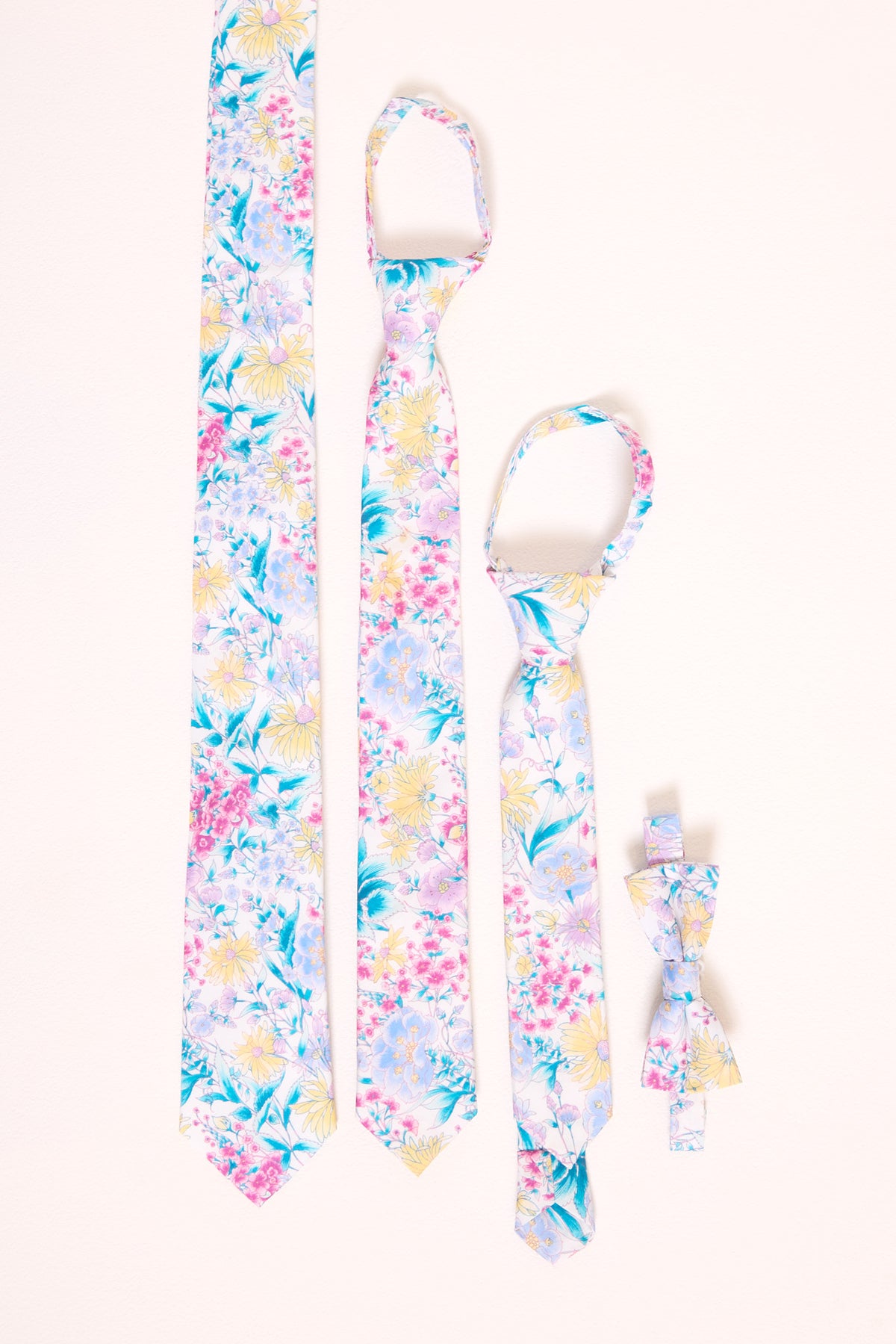 An assortment of floral ties in various sizes laying flat against a white backdrop