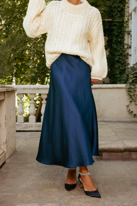 Person wearing a white textured sweater and navy blue skirt outdoors.