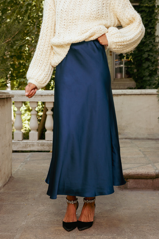 Person wearing a white sweater and blue skirt outdoors.