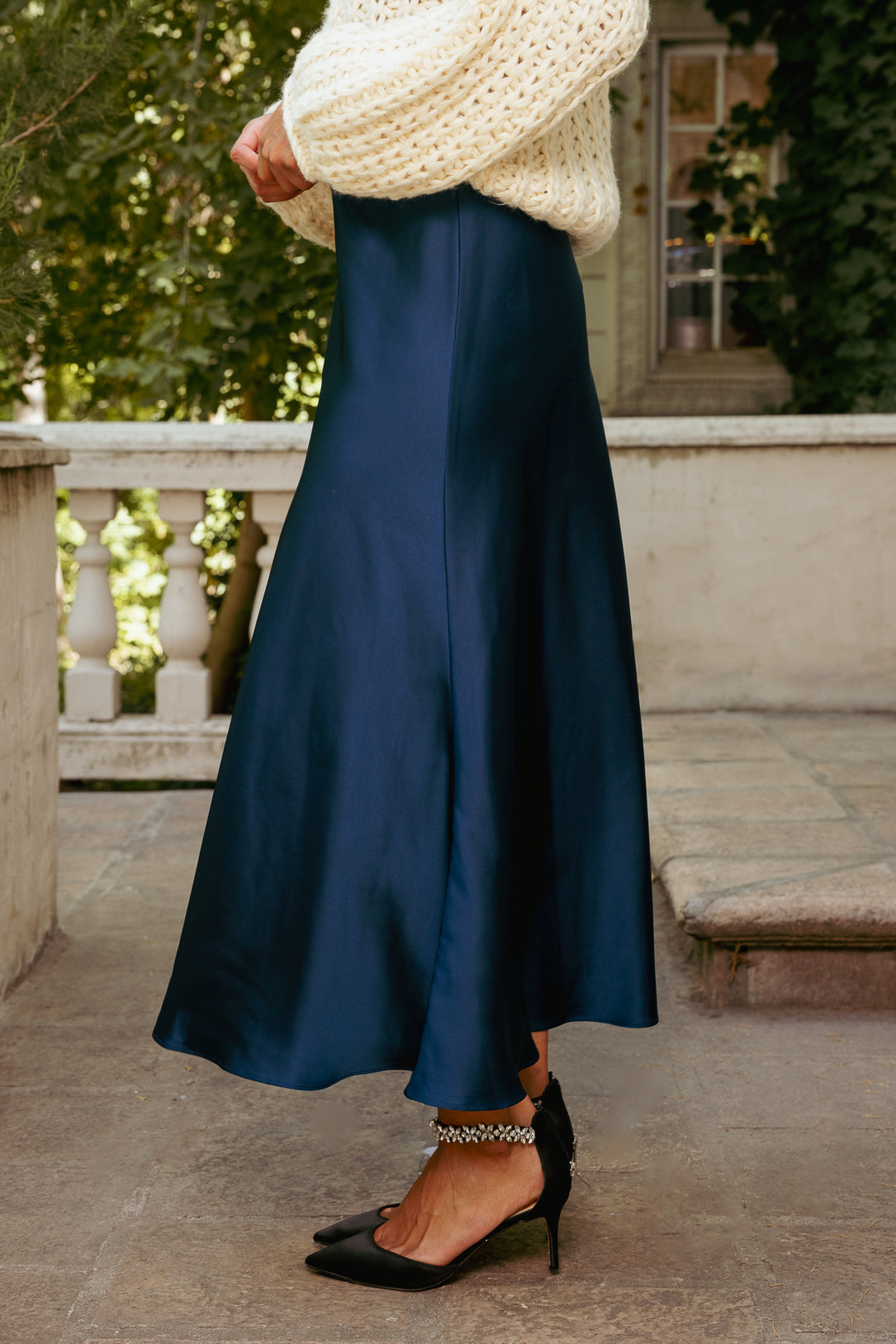 Person wearing a navy blue skirt with a white sweater and black shoes on a stone path.