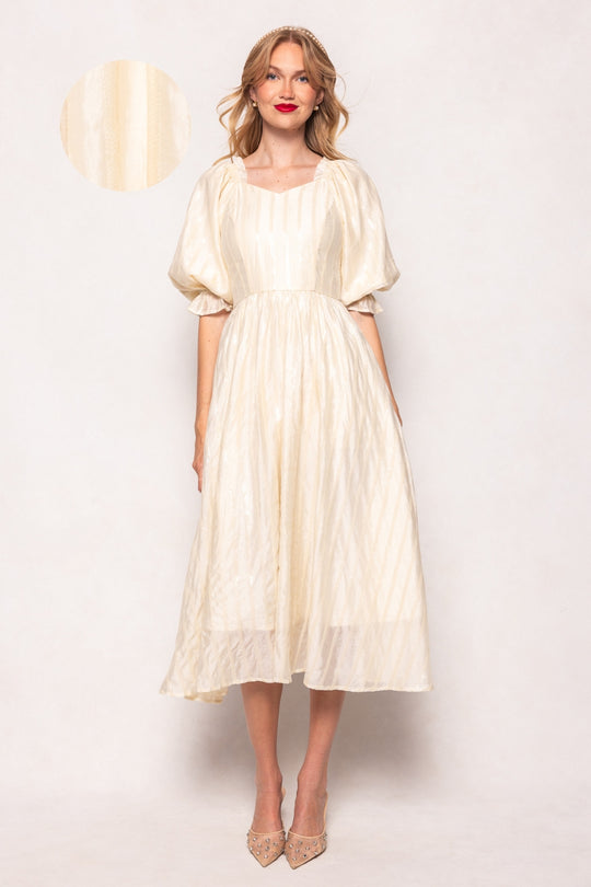 Woman wearing a white dress with sheer sleeves against a plain background