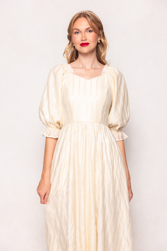 Woman wearing a long, light-colored dress against a plain background