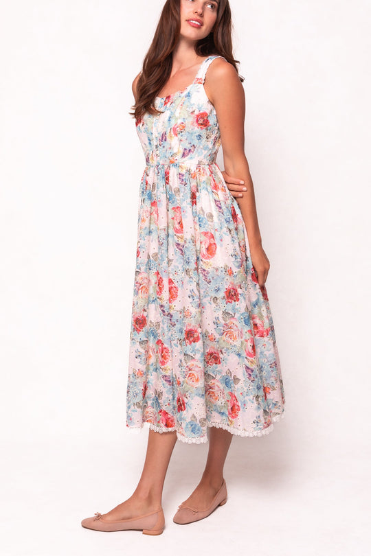 A woman wears the Ivy City Co Penny Tank Midi Dress in Multicolor Floral, featuring a sleeveless design, fitted waist, and a delicate cotton eyelet lace-trimmed hem; she pairs it with nude flats while standing against a plain white background.