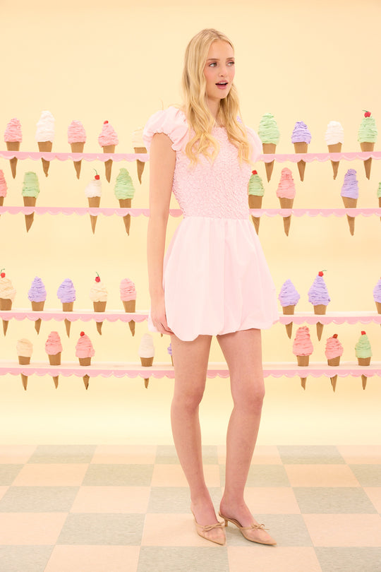 Woman in a pink dress standing in front of an ice cream cone display.