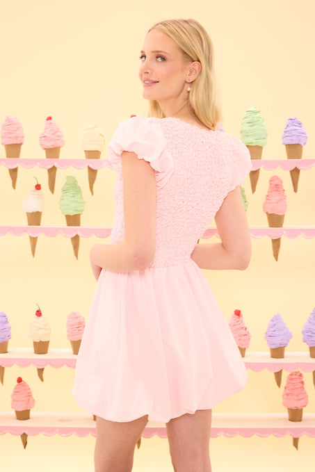 Woman in a pink dress standing in front of a colorful ice cream cone display.