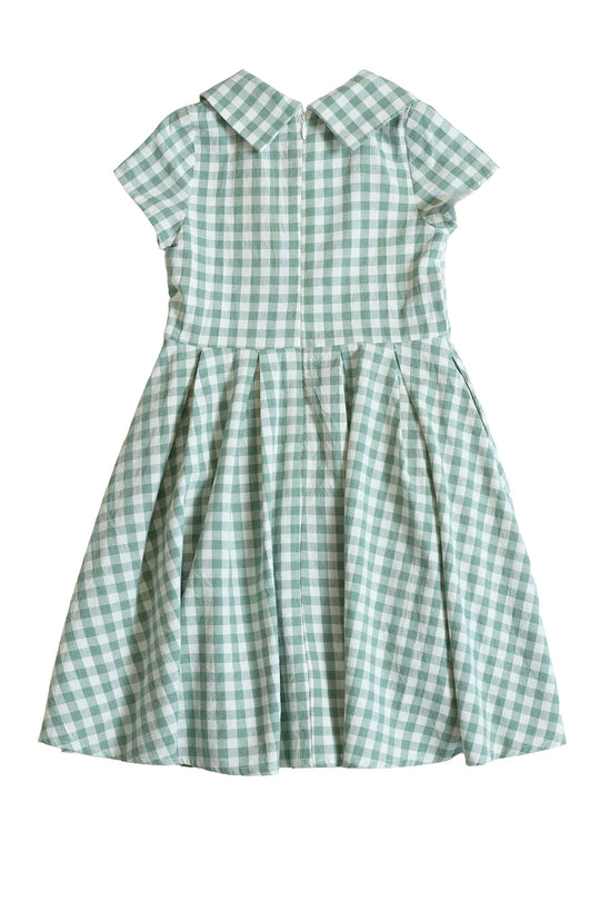 The Mini Amber Dress in Sage Gingham by Ivy City Co is a short-sleeved, knee-length cotton midi dress featuring a green and white sage gingham pattern, pleated skirt, and pointed collar, displayed on a plain white background.