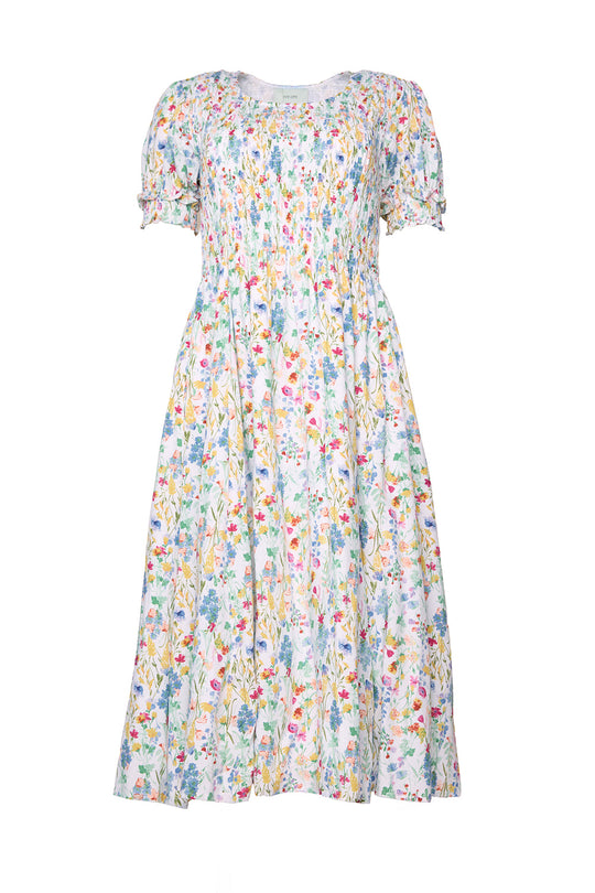 The Amelie Dress in Floral Fields by Ivy City Co is a knee-length midi dress featuring short puff sleeves and a vibrant floral print in blue, yellow, red, and green on a white background. With its gathered bodice and loose, flowing skirt, this comfortable maternity dress is perfect for any occasion.