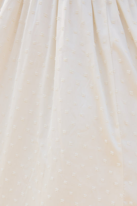Close-up of the cream-colored fabric on the Zella Bow Dress in Ivory by Ivy City Co, featuring a subtle dotted texture and small, raised square patterns. The soft material is slightly gathered, hinting at its elegant design—ideal for a rehearsal dinner or as a modern bridal dress.
