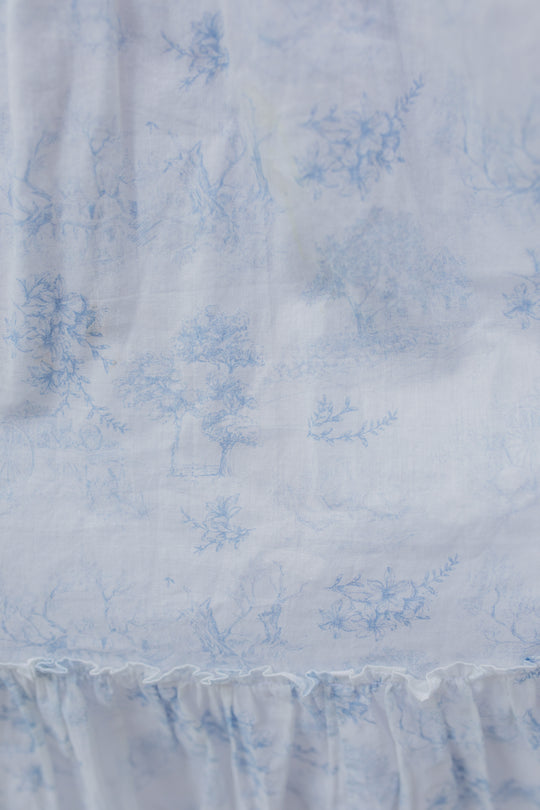 Close-up of light blue pastoral and floral patterns on white cotton fabric with gathered ruffle detail, showcasing the elegant Ivy City Co Valencia Dress—a chic and maternity-friendly style.