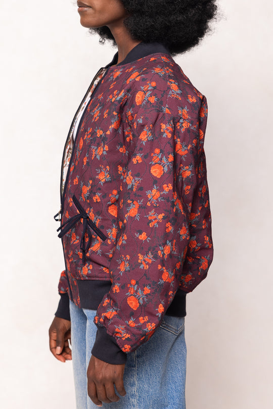Person wearing a floral bomber jacket with orange flowers on a white background