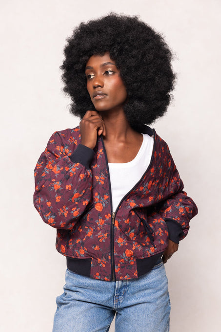 Woman wearing a floral bomber jacket and blue jeans against a plain background