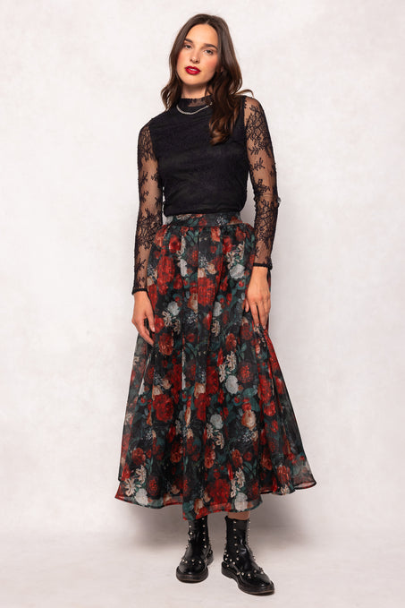 Woman wearing a black top with sheer sleeves and a floral skirt on a white background