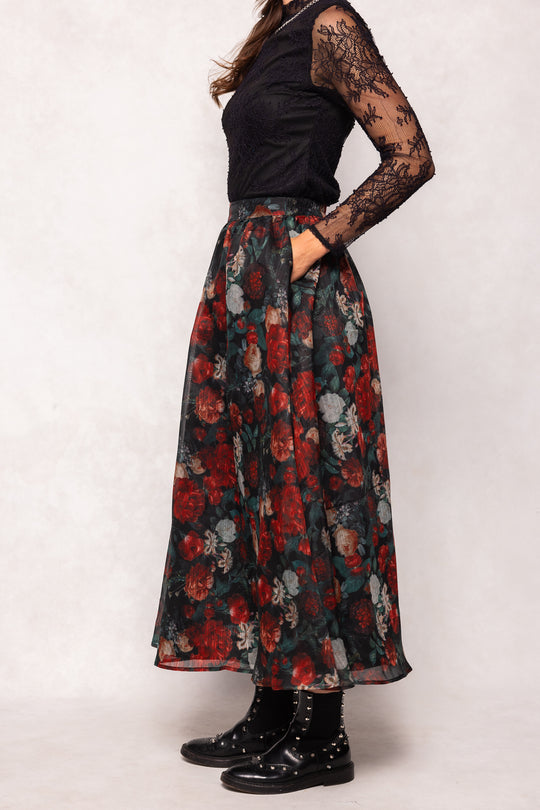 Person wearing a black top and floral skirt on a white background