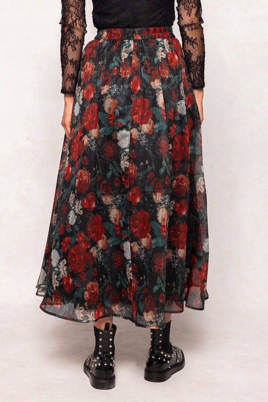 Long floral skirt with red and green pattern worn by a person on a white background