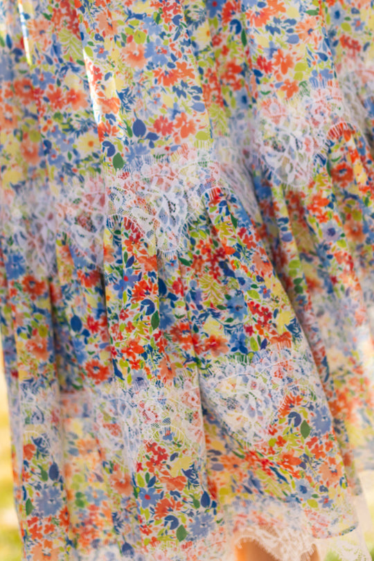 Close-up of the Ivy City Co Verona Skirt in Vibrant Yarrow, showcasing a colorful floral print with small red, orange, blue, and yellow flowers and white lace trim. The light fabric is perfect for a flowing summer look.