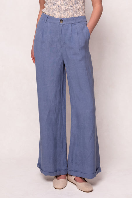 A person wears the Ivy City Co Veronica Pants in Blue—high-waisted, wide-leg linen-blend trousers styled with beige flats and a sleeveless top. Cropped at the shoulders, theyre perfect summer pants for a relaxed fit.