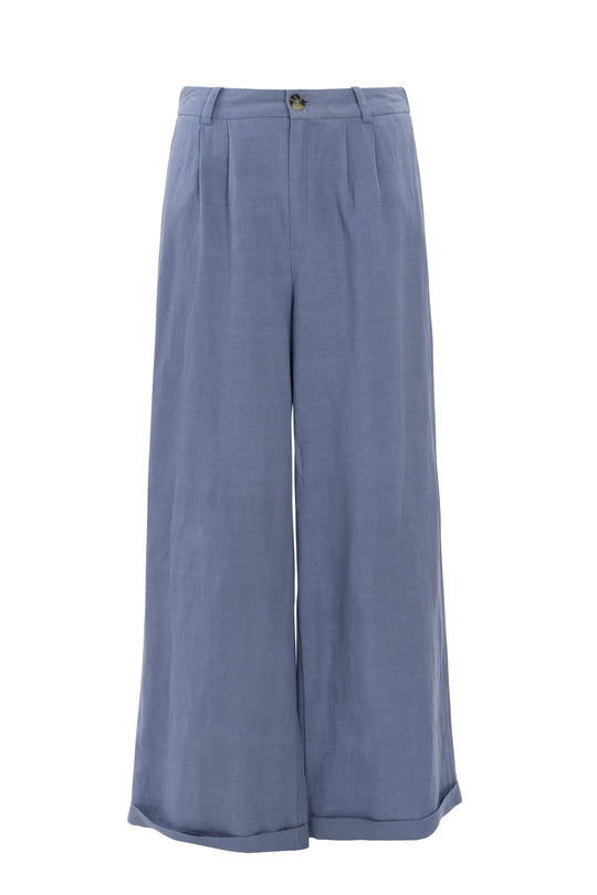 The Veronica Pants in Blue by Ivy City Co are light blue, wide-leg linen-blend trousers with a high waist, front pleats, relaxed fit, zip and button closure, and rolled cuffs—ideal for summer.