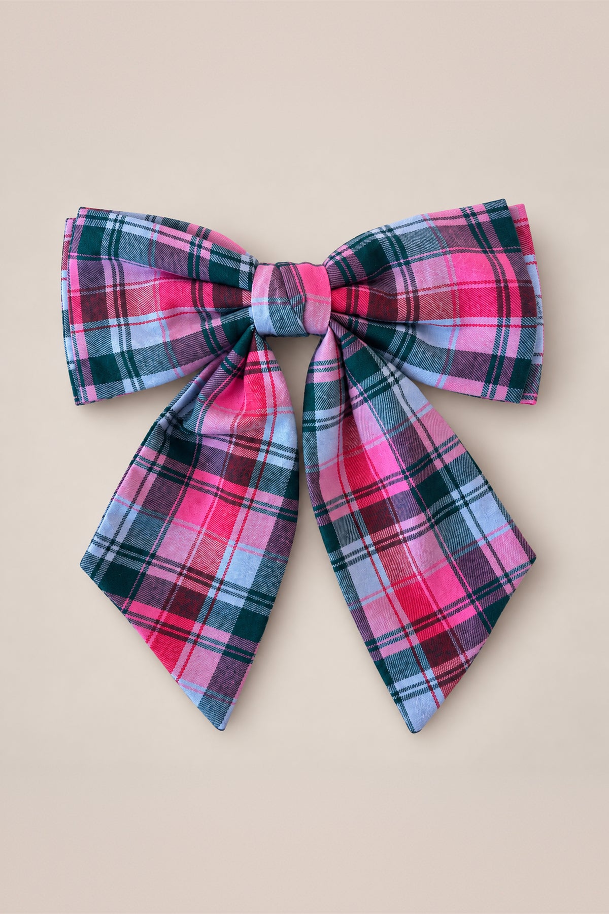Add a touch of festive charm to any outfit with Ivy City Co’s Hair Bows in Vibrant Plaid, featuring a large bow adorned in shades of pink, red, black, and white arranged in a symmetrical pattern—set against a plain beige background for the perfect holiday accessory.