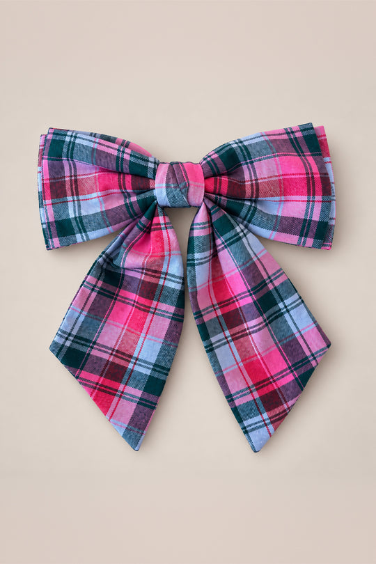 Add a touch of festive charm to any outfit with Ivy City Co’s Hair Bows in Vibrant Plaid, featuring a large bow adorned in shades of pink, red, black, and white arranged in a symmetrical pattern—set against a plain beige background for the perfect holiday accessory.
