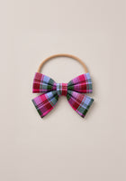 The Hair Bows in Vibrant Plaid by Ivy City Co feature a playful mix of pink, purple, blue, and green plaid fabric on a beige elastic hairband, shown against a light beige background—a delightful holiday accessory to bring festive charm to any outfit.