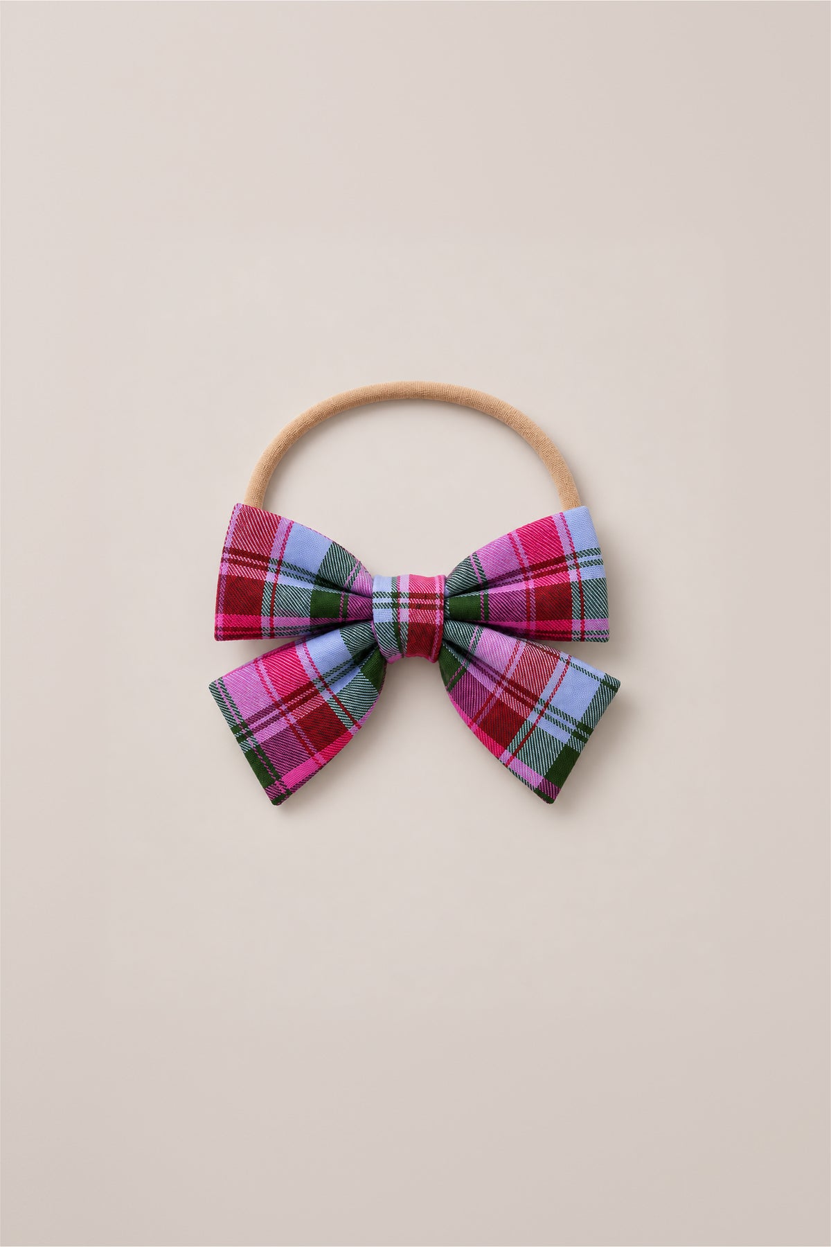 The Hair Bows in Vibrant Plaid by Ivy City Co feature a playful mix of pink, purple, blue, and green plaid fabric on a beige elastic hairband, shown against a light beige background—a delightful holiday accessory to bring festive charm to any outfit.