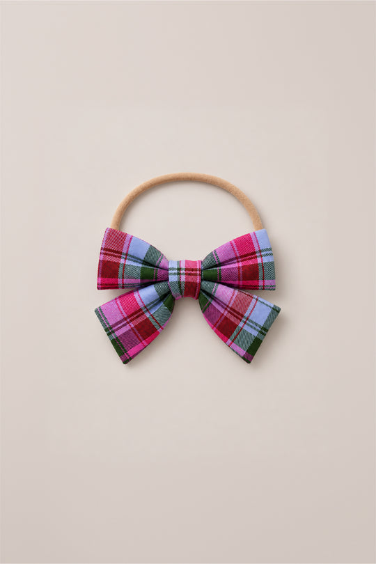 The Hair Bows in Vibrant Plaid by Ivy City Co feature a playful mix of pink, purple, blue, and green plaid fabric on a beige elastic hairband, shown against a light beige background—a delightful holiday accessory to bring festive charm to any outfit.