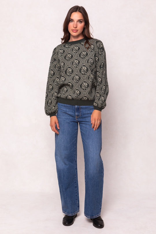 Woman wearing a patterned sweater and blue jeans on a white background