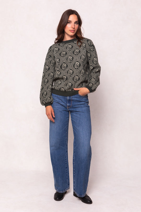 Woman wearing a patterned sweater and blue jeans on a white background