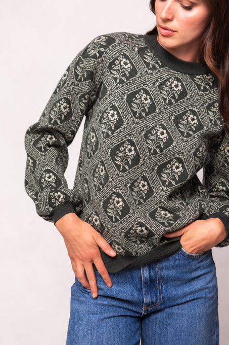 Person wearing a patterned sweater and blue jeans against a plain background