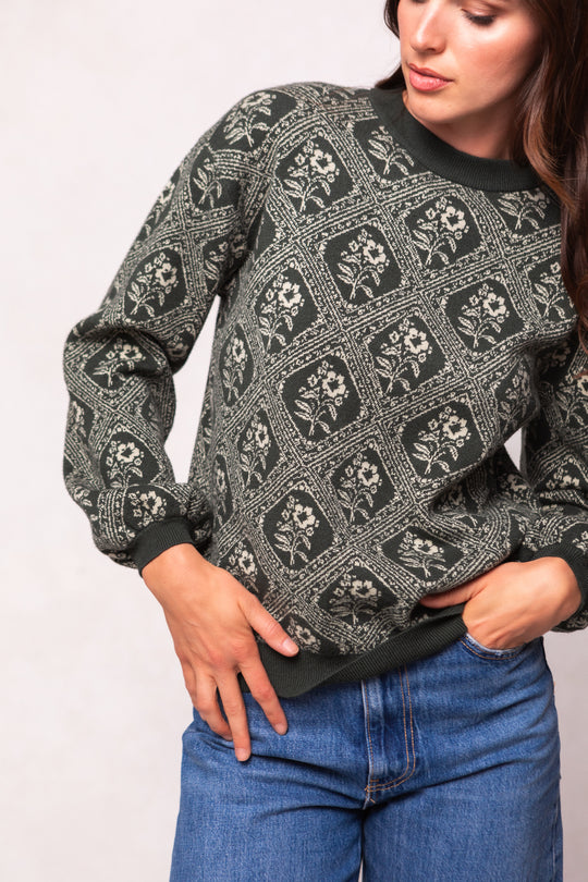 Person wearing a patterned sweater and blue jeans against a plain background