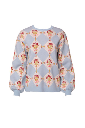 The Vivienne Sweater in Mosaic Bloom by Ivy City Co features a diamond pattern with alternating blue and white sections, accented by red and yellow florals on white tiles. Ribbed cuffs and hem complete this maternity-friendly style.