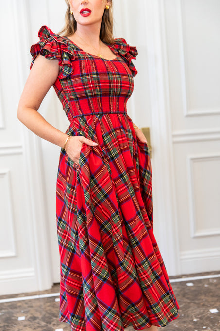 Woman wearing a red plaid dress with ruffled shoulders against a white wall.