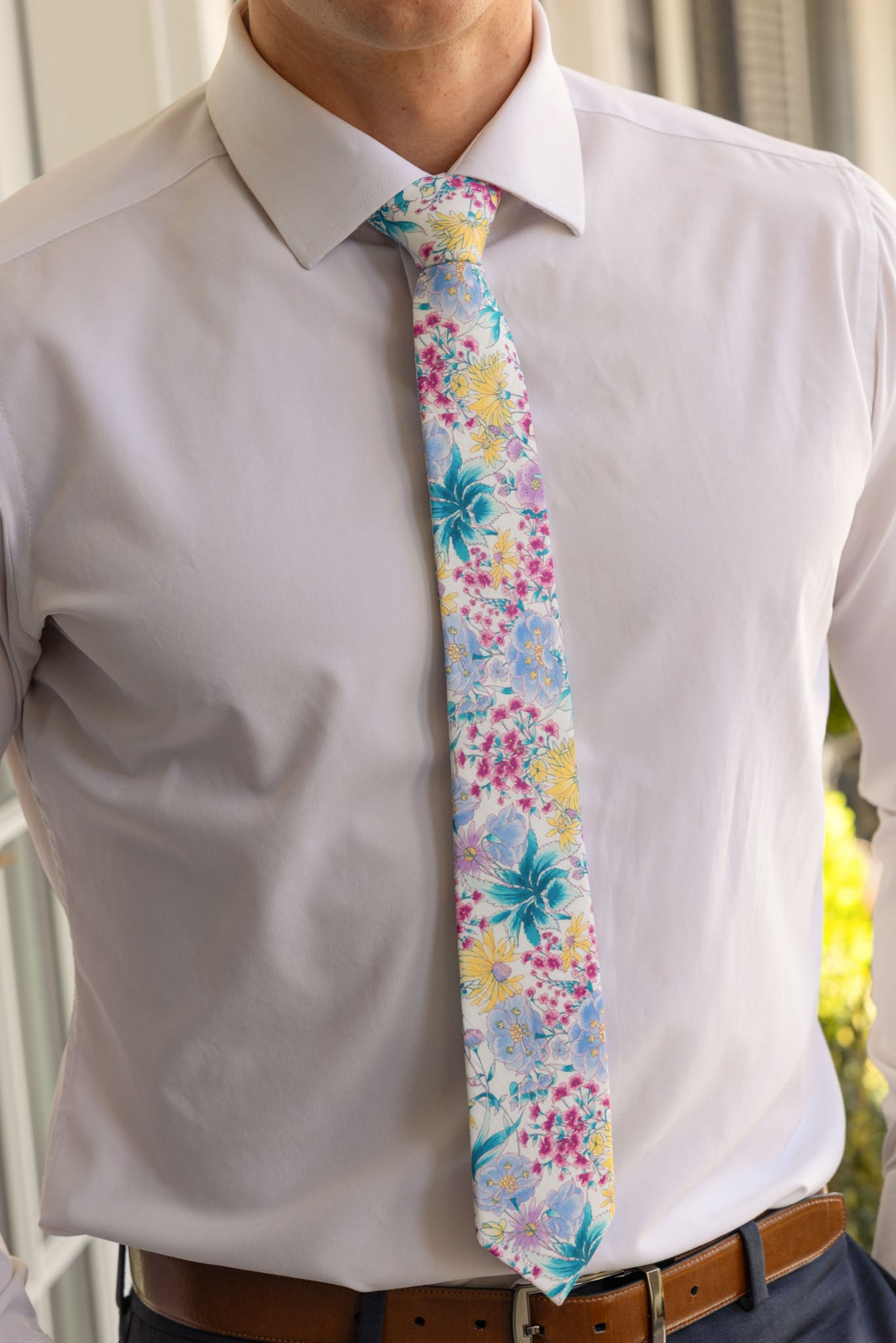 Wearing a white dress shirt, navy pants, and Ivy City Co’s Ties in Pretty Plumeria—a light blue floral tie with yellow, pink, and blue flowers—creates a formal yet summery look that's perfect for spring celebrations.
