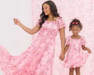 Woman and child in matching pink floral dresses standing on a pink floral background