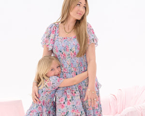 Woman and child wearing matching floral dresses in a pink room.