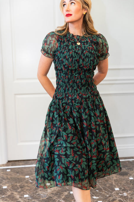 Woman wearing a green floral dress against a white wall.
