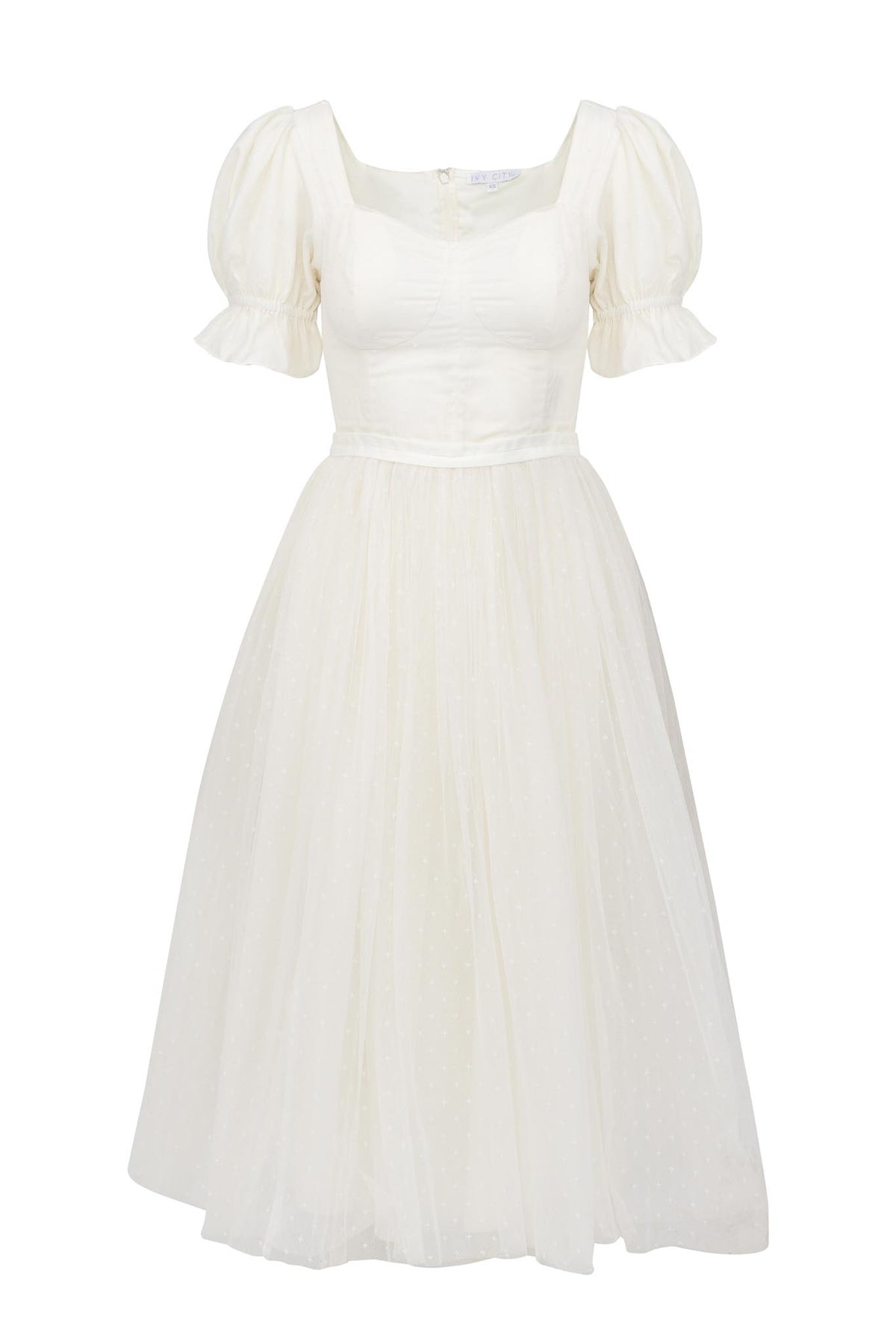 The Ivy City Co Ballerina Dress in White features puffed short sleeves, a fitted bodice, square neckline, and flared skirt with subtle polka dots—ideal for a dreamy ballerina-inspired look.