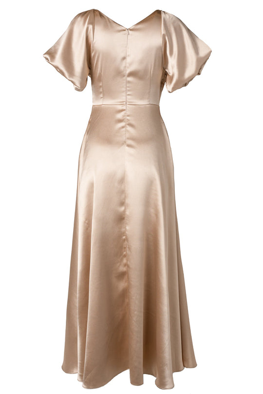 The Tessie Dress in Champagne by Ivy City Co is crafted from satin and features short flutter sleeves, a fitted waist, and a flattering V-neckline. Its long, slightly flared skirt makes it an elegant choice for bridesmaids or wedding guests.